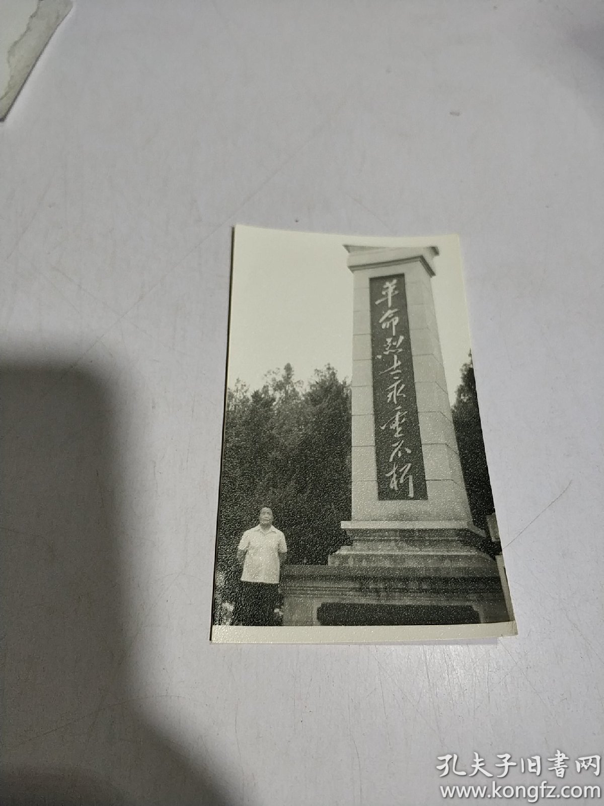 黑白老照片:一人留影照,背景有革命烈士永垂不朽