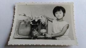 早期厚相纸电视机旁的小美女黑白照片。