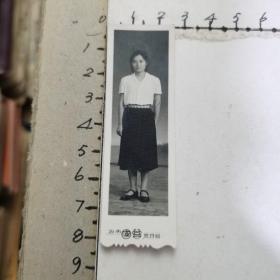 老照片：穿白短袖、黑裙、系花边腰带的女青年（60’70年代、竖式、尺寸：2.5×8.2cm）