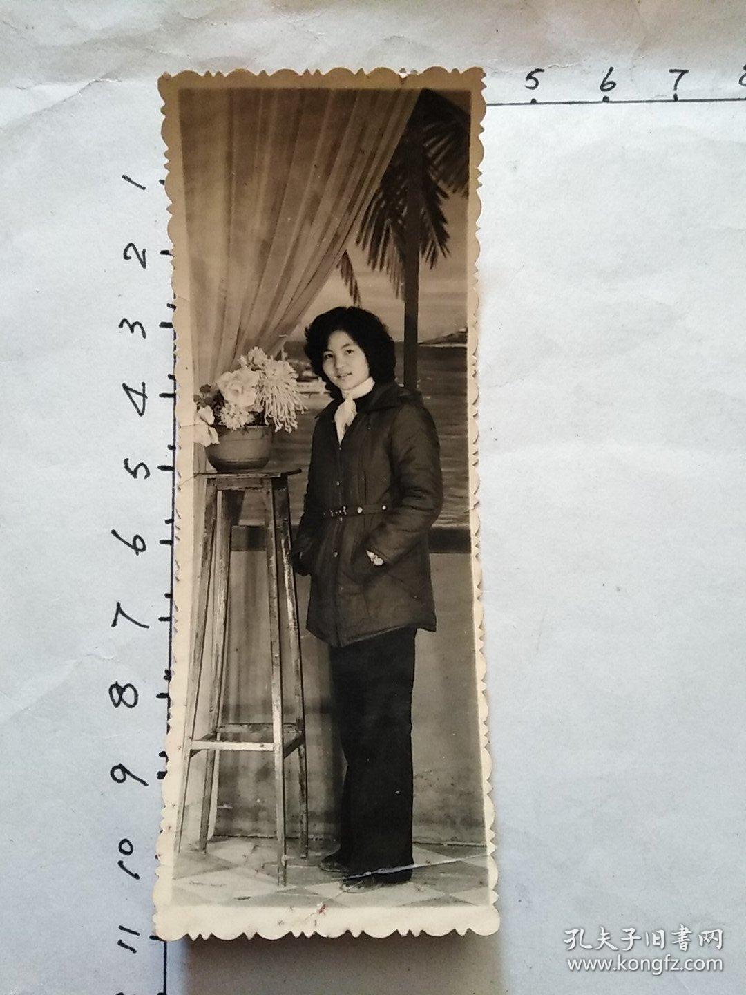 80年代竖式老照片:一位系纱巾戴手表女青年双手插菏包在菊花盆景旁