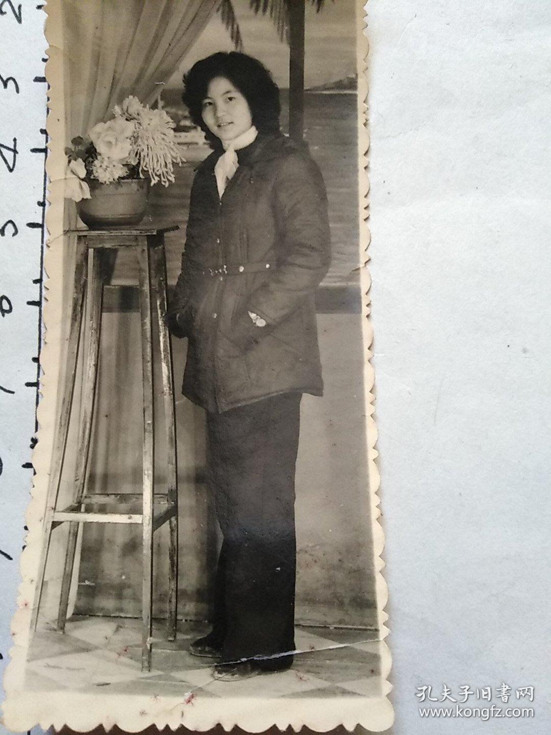 80年代竖式老照片:一位系纱巾戴手表女青年双手插菏包在菊花盆景旁